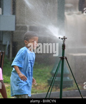 Young African American Boy Spielen an einem Wasser Sprinkler in einem Stadtpark, Bronx, New York, USA, 4. August 2010 © Katharine Andriotis Stockfoto