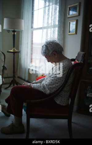 Alte Frau sitzt im Stuhl mit gesenktem Kopf Stockfoto
