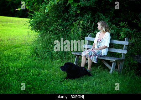 Frau sitzt auf der Bank mit schwarzer Labrador Hund neben Stockfoto