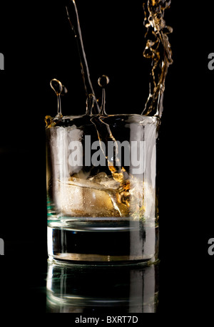 Glas Whiskey auf einem schwarzen Hintergrund. Whisky-Spritzer in ein Glas. Whisky mit Eis. Stockfoto