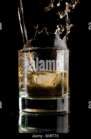 Glas Whiskey auf einem schwarzen Hintergrund. Whisky-Spritzer in ein Glas. Whisky mit Eis. Stockfoto