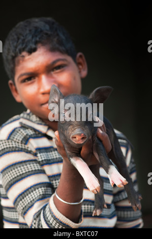 Untere Kaste indischer Junge mit kleinen Schwein, das von ihm aufgezogen wird und verkauft für Fleisch, wenn völlig gewachsen. Andhra Pradesh, Indien Stockfoto