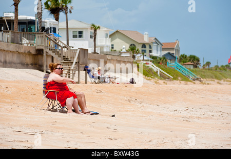 Übergewichtige Frau in roten sitzen auf Stuhl Sonnenbad am Beverly Beach, Florida Stockfoto