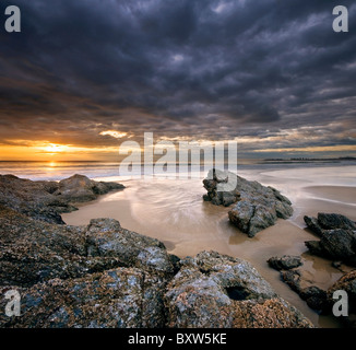 Felsen am Strand bei Sonnenaufgang mit dramatischer Himmel auf ein quadratisches format Stockfoto