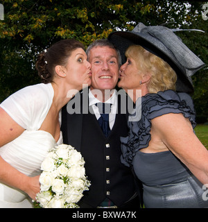 Quadratische Nahaufnahme Spaß Porträt von einem Bräutigam an seinem Hochzeitstag immer einen Kuss auf beide Wangen von seiner neuen Braut und Schwiegermutter. Stockfoto