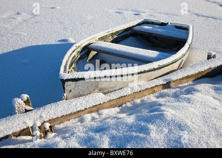 Kleines Ruderboot, bedeckt mit Schnee und Raureif am Rand von einem Bootfahren Teich, Schottland Stockfoto