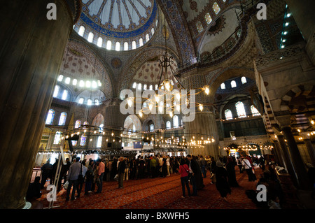Blaue Moschee Innere Touristen Istanbul Türkei // ISTANBUL, Türkei - Touristen bevölkern Istanbuls berühmte Blaue Moschee. Das Innere der Moschee ist bekannt für seine atemberaubenden blauen Fliesen, die komplizierte Kalligraphie und die beeindruckenden Kuppeln, die eine atemberaubende Atmosphäre für Besucher schaffen. Sultan-Ahmed-Moschee (türkisch Sultanahmet Camii), im Volksmund als Blaue Moschee bekannt, ist eine muslimische (sunnitische) Moschee im Zentrum von Istanbuls Altstadt von Sultanahmet. Sie wurde von Sultan Ahmed I. in Auftrag gegeben und 1616 fertiggestellt. Stockfoto