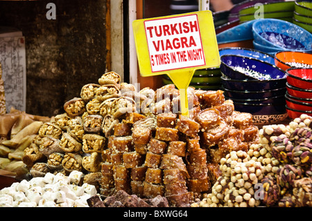 Gewürzbazar-Türkische Süßigkeiten-Werbung Istanbul Türkei | ISTANBUL, Türkei — Ein scherzhaftes Schild mit der Aufschrift „Türkisches Viagra“ steht zwischen Haufen getrockneter Feigen, Walnüssen und Türkischer Süßigkeit auf dem Stand eines Händlers im Gewürzbazar (Mısır Çarşısı). Der Bazar, der Anfang der 1660er Jahre als kommerzieller Anbau des Yeni-Camii-Komplexes erbaut wurde, hat sein Ladenangebot seit Ende des 20. Jahrhunderts von Gewürzen und Apothekenwaren hin zu Süßwaren, Keramik und Souvenirs für eine internationale Kundschaft verlagert. Stockfoto