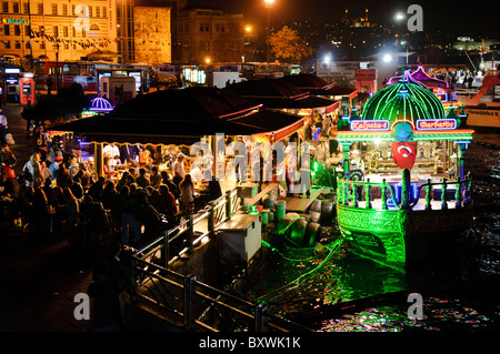 Balik Ekmek schwimmende Restaurants Eminonu Istanbul // ISTANBUL, Türkei - beleuchtete balik Ekmek Boote servieren traditionelle Fisch-Sandwiches an der Eminonu Uferpromenade in der Nähe der Galata Brücke. Diese schwimmenden Restaurants, die in der Region als balıkçı tekneleri bekannt sind, bieten gegrillte Makrele in Weißbrot mit Zwiebeln und Salat als beliebtes Street Food an. Die kunstvoll verzierten Boote sind im osmanischen Stil gehalten und bleiben dauerhaft an der historischen Wasserfront des Goldenen Horns verankert. Eminonu dient als wichtiger Fährhafen und Geschäftsviertel, der die europäische und asiatische Seite von ist verbindet Stockfoto