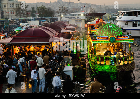 ISTANBUL, Türkei / Türkiye – Eminonu-Ufer in Istanbul bei Sonnenuntergang. Am Ufer des Goldenen Horns neben der Galata-Brücke ist ein beliebter Ort, um gegrillte Fisch-Sandwiches zu erhalten, die auf den Booten zubereitet werden, die auf dem Wasser neben dem Dock wippen. Stockfoto