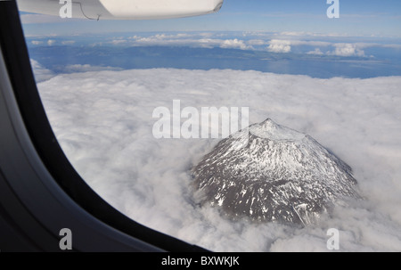 Aus der Vogelperspektive des schneebedeckten Mount Pico, der sich über den Wolken erhebt, von einem Flugzeugfenster aus gesehen, mit der Insel São Jorge im Hintergrund, Azoren, Portugal Stockfoto
