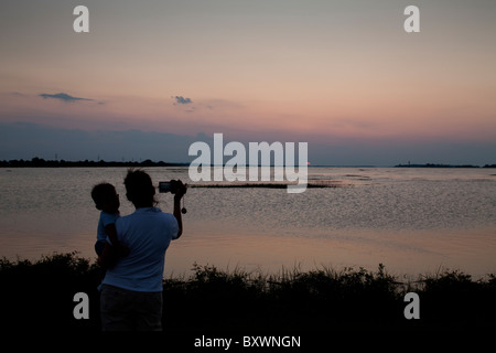 USA, Georgia, Tybee Island, Frau, hält, Baby video der untergehende Sonne in Tidewater nimmt Bucht entlang der Küste am Sommerabend Stockfoto