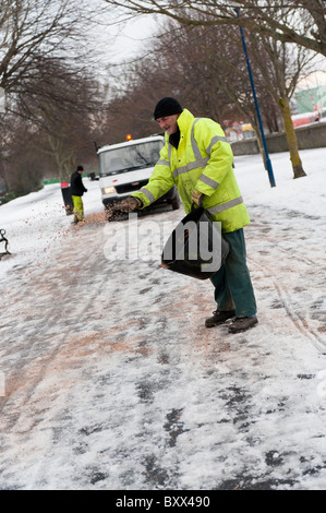 ein Rat Kommunalbeschäftigten verbreiten Sand und Salz von Hand auf eisigen Fußweg zu einer Schule, Wales UK Stockfoto