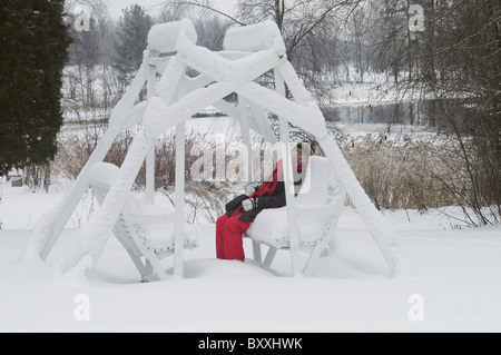 Frau sitzt auf einem hölzernen schwingen mit unberührten Schnee bedeckt Stockfoto
