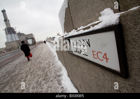 Fußgänger auf der schneebedeckten Londoner Brücke mit Straßenschild und dem Glasscherbenturm, der im Hintergrund gebaut wird Stockfoto