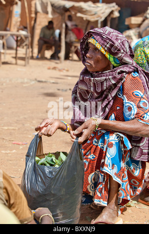 In der Stadt Djibo im nördlichen Burkina Faso hält ein älterer Fulbe-Frau auf dem Markt, Grüns für das Abendessen zu kaufen. Stockfoto