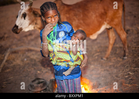 Fulani-Mädchen und Kind in der saisonalen Dorf Pete Goonga im nördlichen Burkina Faso.  Ein Kochen Feuer brennt auf der Rückseite. Stockfoto