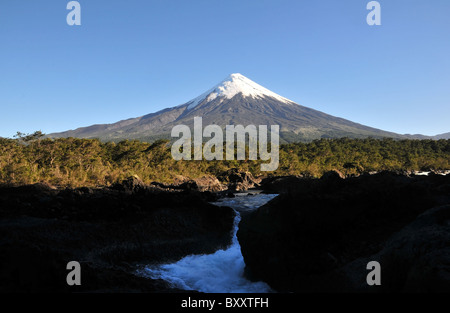 Blauer Himmelsblick auf Volcan Osorno erhebt sich über gemäßigten valdivianischen Regenwald und Wildwasser Petrohue Wasserfall Cascade, Chile Stockfoto