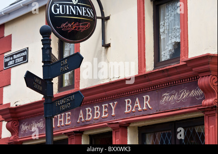 Wegweiser zum Gardasee und Parkplatz neben Guinness-Werbung in der Abtei Bar in Abbey Street, Timoleague, West Cork, Irland Stockfoto