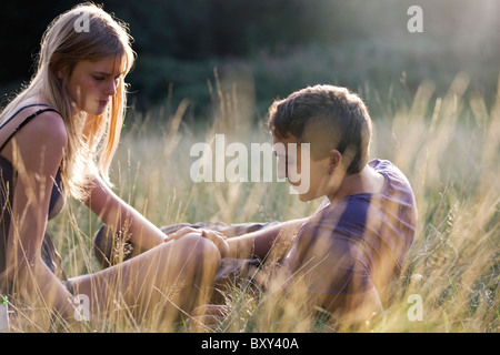 Ein junges Paar, sitzen in der Wiese, mans Hand auf das Knie womans Stockfoto