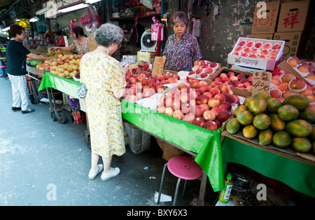 Eine Frau kauft Obst-Verkäufer bei einem Obstmarkt in zentralen Taipei steht hinter dem Tisch bestückt mit reifen Äpfeln, Mangos etc. Stockfoto