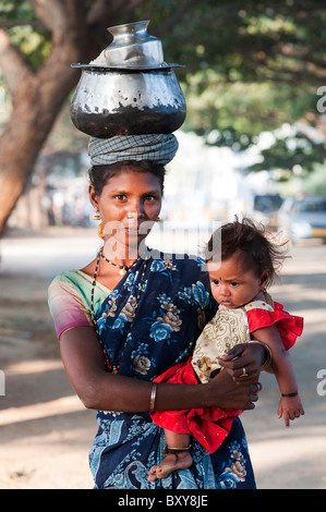 Armen niedrigere Kaste indische Frau mit Baby mit einem Topf Reis auf dem Kopf. Andhra Pradesh, Indien Stockfoto