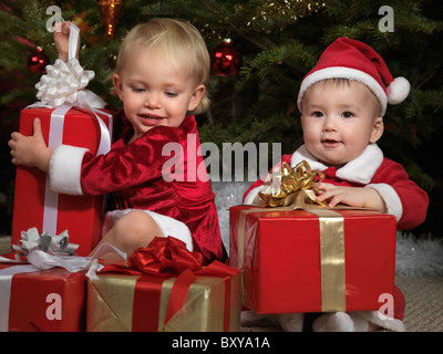 Zwei Jahre altes Mädchen und eine acht Monate alte junge öffnen ihre Geschenke unter einem Weihnachtsbaum Stockfoto