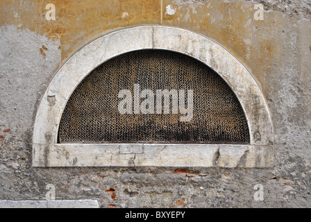 halbmondförmige Fenster mit Sicherheitsnetz und die Mauer bröckelt Stockfoto