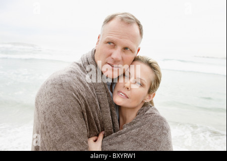 Umarmt paar fallenden Decke Wegschauen am Strand Stockfoto