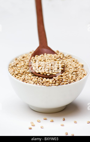Nahaufnahme einer Schüssel voller Gerste und Kochlöffel auf weißem Hintergrund Stockfoto