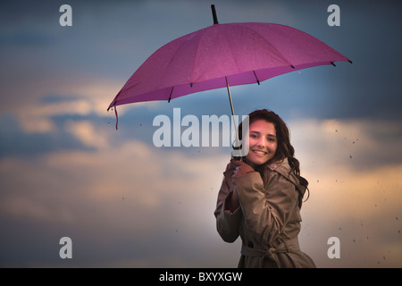 Junge Frau mit Regenschirm unter bewölktem Himmel Stockfoto