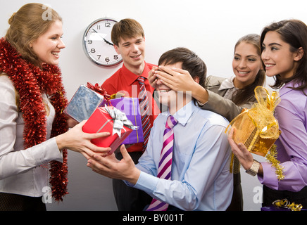 Foto von fröhlichen Geschäftsfrau, halten sie die Hände auf den Augen des Mannes während ihrer Kollegen bereitet Geschenke für ihn Stockfoto