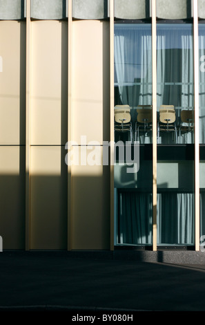 Die Sonne wirft einen Schatten auf ein Gebäude mit Glasscheiben in einer Stadtstraße mit Stühle gestapelt innerhalb des Fensters. Stockfoto