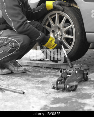 Ein Mechaniker die Radmuttern mit einem Schraubenschlüssel abschrauben, das Rad von einem Auto, Rigger Handschuhe zum Schutz zu entfernen. Stockfoto