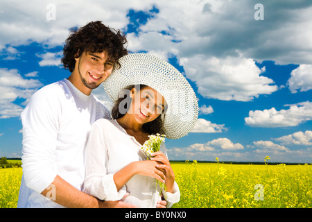 Foto des glücklichen Kerl umarmt seine Freundin mit Blumenstrauß beim stehen auf der Wiese im Sommer Stockfoto