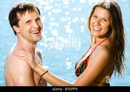 Porträt der glückliche Frau im Bikini, legte ihre Hand auf ihr Ehemann Schulter während beide Blick in die Kamera auf Hintergrund blau Stockfoto