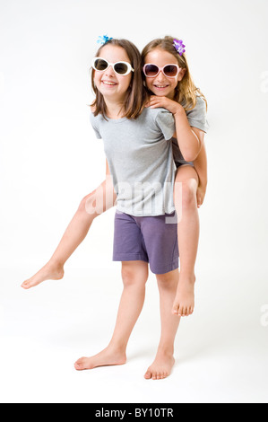 Zwei Mädchen mit Sonnenbrille mit Spaß ein Mädchen nehmen die andere eine Huckepack isoliert auf weiss Stockfoto