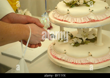 Eine Nahaufnahme von einer Braut & Bräutigam Hände, wie sie schneiden die Hochzeitstorte an der Rezeption Stockfoto