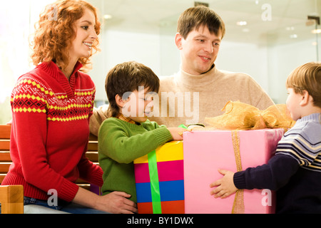 Glückliche Eltern auf ihre Kinder, während sie versuchen, die Geschenke auspacken Stockfoto