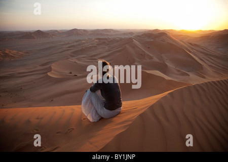 Oman, Khali. Eine junge Frau beobachtet den Sonnenuntergang über den Dünen. MR. Stockfoto