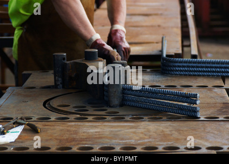 Konkrete Verstärkung: Stahl, Betonstahl geschnitten und gebogen Fabrik. Arbeiter biegen Stahlstangen Stockfoto