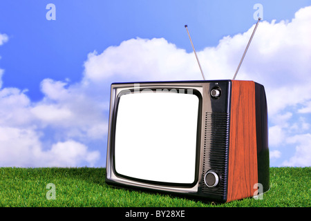 Foto von einem alten Retro-TV im Freien auf dem Rasen mit blauem Himmel und weißen Wolken im Hintergrund Stockfoto