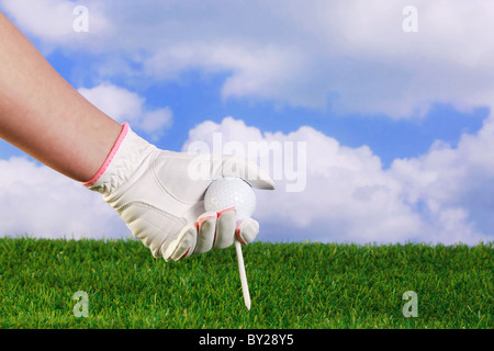 Foto einer Damen Hand in weiß und rosa Handschuh indem ein Golfball und Abschlag in Rasen. Stockfoto