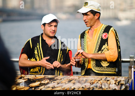 Balik Ekmek Fish Sandwich Street Food Eminonu Istanbul // ISTANBUL, Türkei – Ein Straßenverkäufer grillt frischen Fisch am Ufer von Eminonu in der Nähe der Galata-Brücke und bereitet das traditionelle balik ekmek (Fisch-Sandwich) zu. Der balik ekmek, der typischerweise aus gegrillter Makrele in Weißbrot mit Zwiebeln und Salat zubereitet wird, gehört zu den beliebtesten Street Food-Gerichten Istanbuls. Fischverkäufer am Wasser bedienen sich seit Generationen von schwimmenden Booten und Ständen entlang des Goldenen Horns. Der Stadtteil Eminonu dient als wichtiger Fährhafen und Handelsknotenpunkt zwischen Istanbuls europäischem und ASI Stockfoto