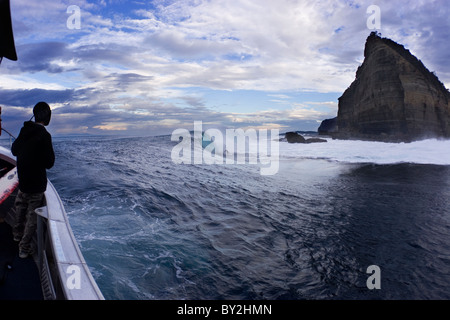 Ein junger Mann schaut aus dem Boot während einer anderen surft eine große Welle an Shipsterns Bluff, in Tasmanien, Australien Stockfoto