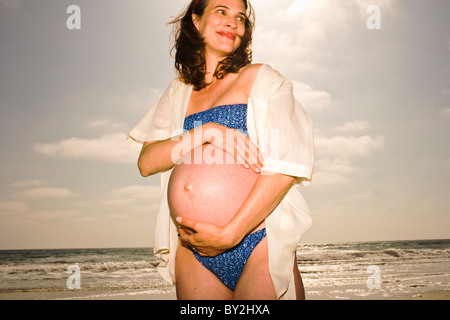 Eine schwangere Frau im Bikini posiert für ein Porträt am Strand. Stockfoto