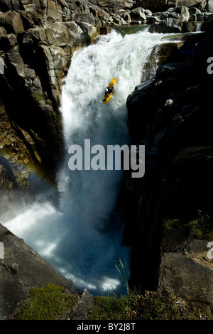 Männliche Kajakfahrer fallen aus einem 60 Fuß Wasserfall in einen Regenbogen. Stockfoto