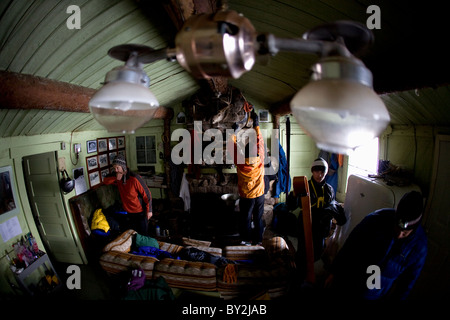 Vier männliche Skifahrer Vorbereitungen zum Skifahren in einer urigen Almhütte mit eine alte Öllampe im Vordergrund. Stockfoto