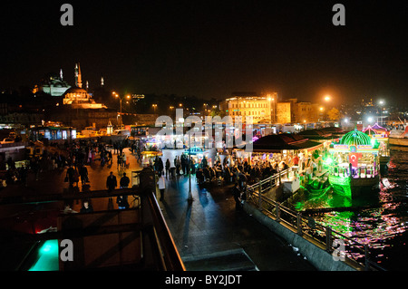 Balik Ekmek Fish Sandwich Boote Eminonu Istanbul // ISTANBUL, Türkei - beleuchtete balik Ekmek Boote servieren traditionelle Fisch Sandwiches an der Eminonu Uferpromenade in der Nähe der Galata Brücke. Diese schwimmenden Restaurants, die in der Region als balıkçı tekneleri bekannt sind, bieten gegrillte Makrele in Weißbrot mit Zwiebeln und Salat als beliebtes Street Food an. Die kunstvoll verzierten Boote sind im osmanischen Stil gehalten und bleiben dauerhaft an der historischen Wasserfront des Goldenen Horns verankert. Eminonu dient als wichtiger Fährhafen und Geschäftsviertel, der die europäische und asiatische Seite der ISTA verbindet Stockfoto