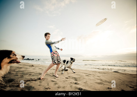 Ein Jugendlicher wirft einen Frisbee für zwei eifrige Hunde an einem ruhigen Strand in Mexiko. Stockfoto